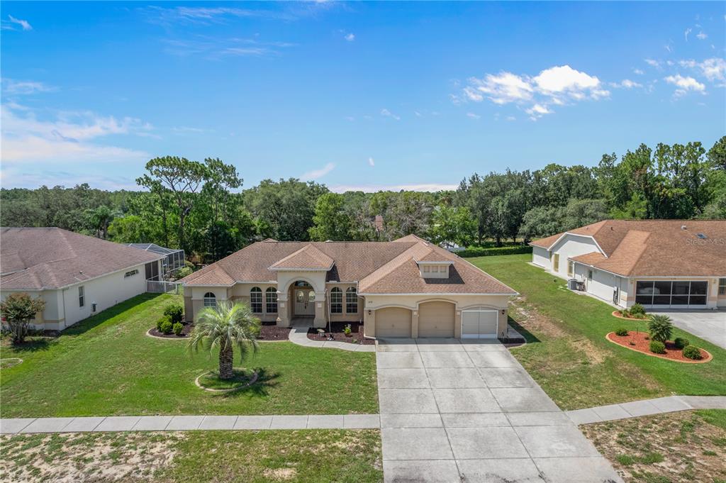 An aerial view shows a single-story suburban house with a three-car garage and lawn — 6132 KRISTA DRIVE, SPRING HILL, FL