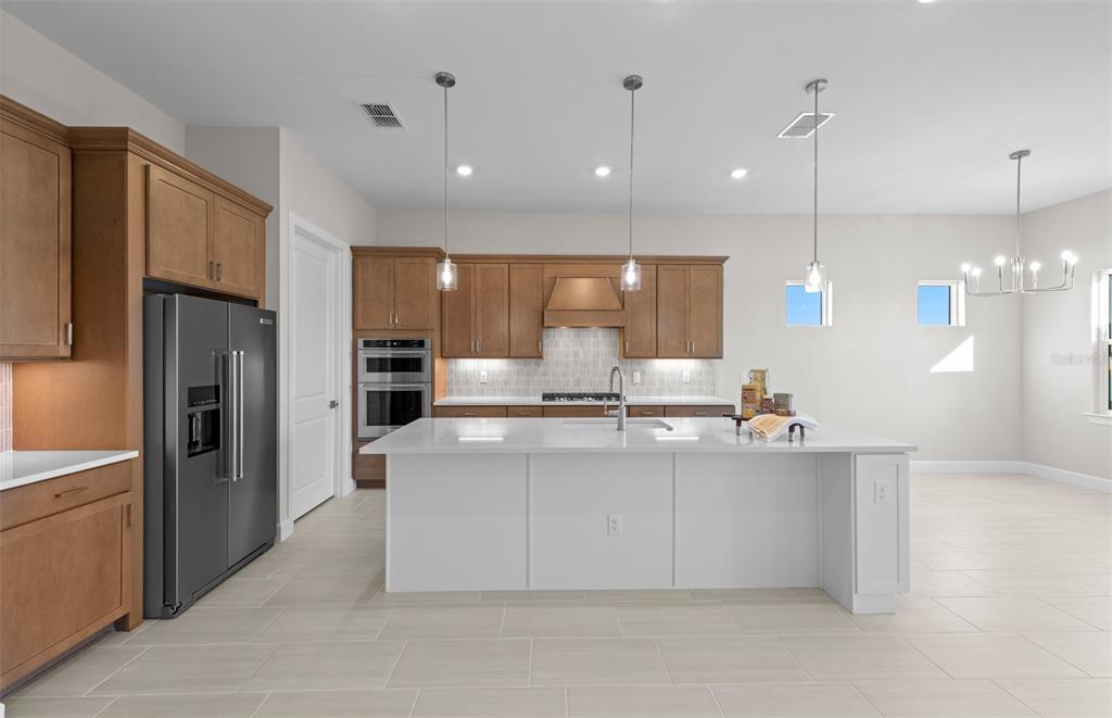 A modern kitchen features wood cabinets, a white island, stainless steel appliances, and tile flooring — 1835 SILVER SHORES BOULEVARD, ENGLEWOOD, FL
