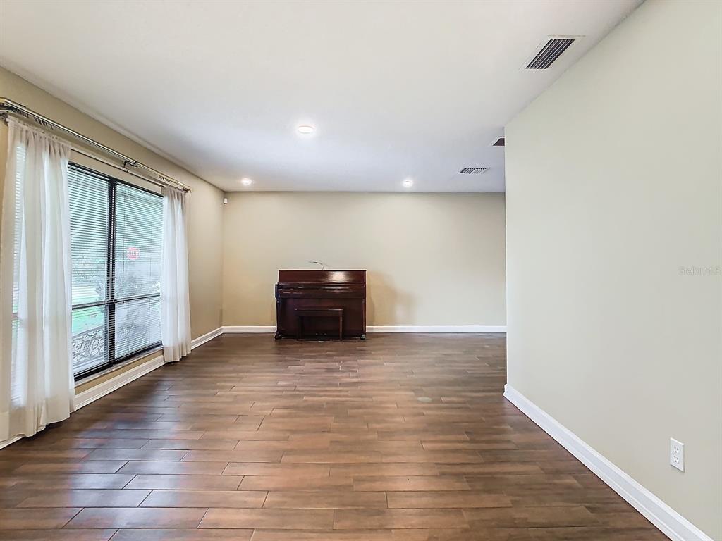 A living room with wood-look flooring, a piano, and large windows with white curtains — 1469 GRACE LAKE CIRCLE, LONGWOOD, FL