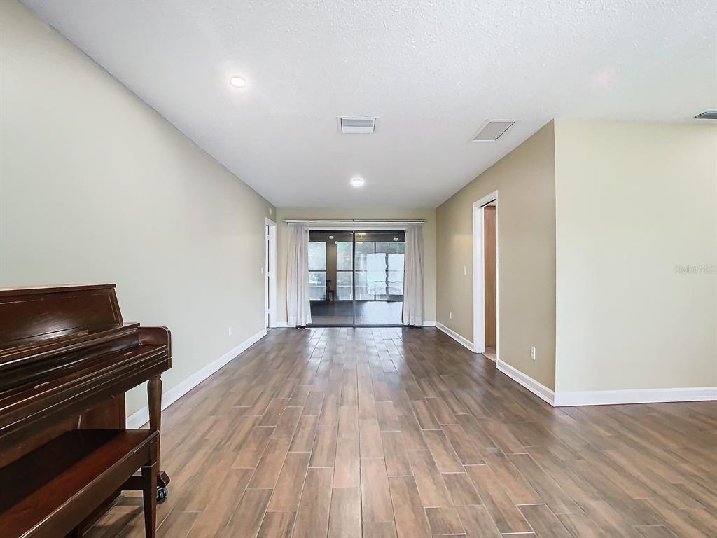 A living room features wood-look tile flooring, a piano, and sliding glass doors to a patio — 1469 GRACE LAKE CIRCLE, LONGWOOD, FL