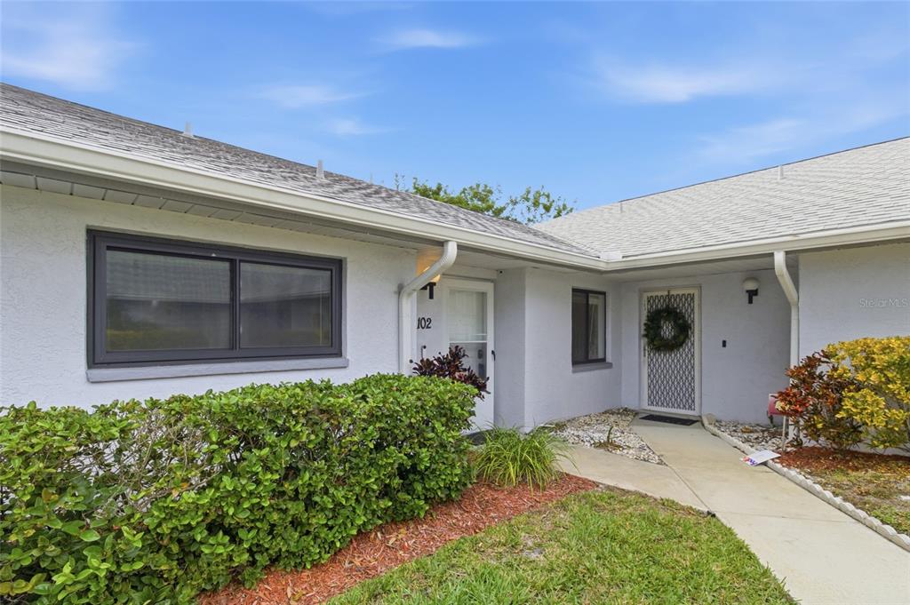 The exterior of a white stucco building features two entry doors and a landscaped yard — 2701 COUNTRYSIDE BOULEVARD UNIT 102, CLEARWATER, FL