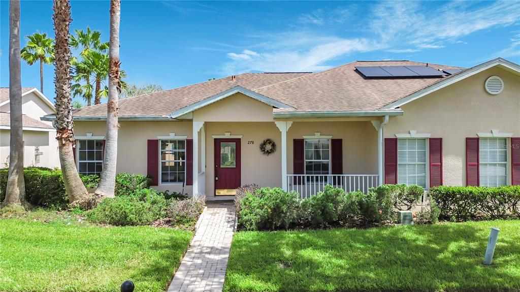 A single-story house with a red front door, maroon shutters, and solar panels on the roof — 278 ANASTASIA DRIVE, KISSIMMEE, FL