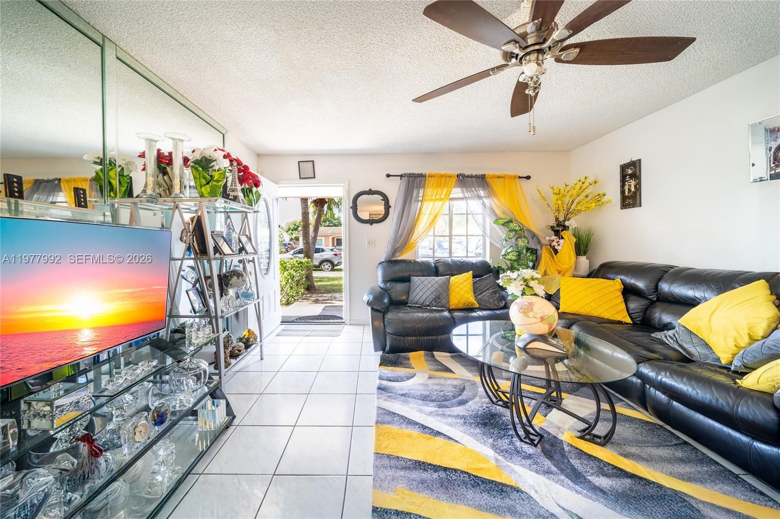 A living room features a black leather sectional, yellow accents, tile flooring, and a ceiling fan — 419 SW 80th Ave, Pompano Beach FL 33068, POMPANO BEACH, FL