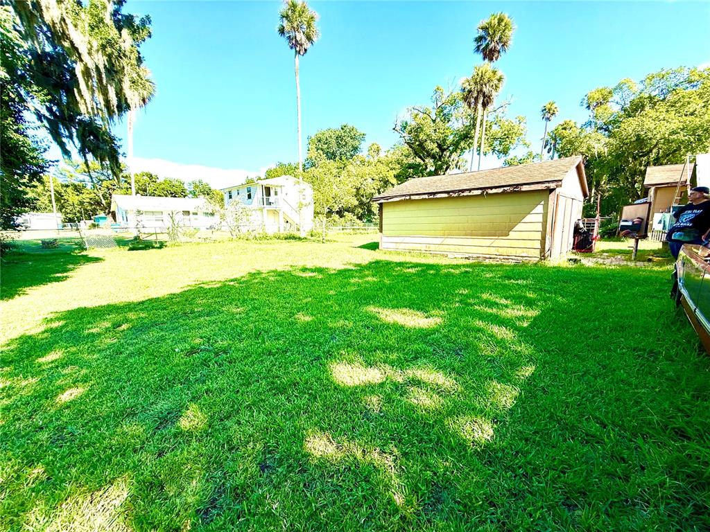 A large, grassy backyard features a detached garage, palm trees, and neighboring houses — 631 ELM AVENUE, HOLLY HILL, FL