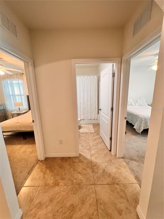 A hallway with tiled flooring leads to a bathroom flanked by two bedrooms — 1267 IGUANA LOOP, DAVENPORT, FL