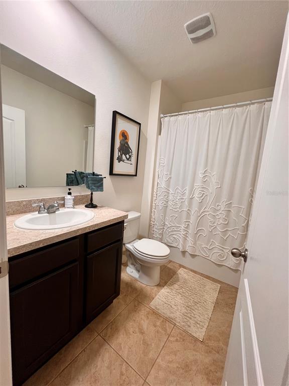 A bathroom features a dark wood vanity, a beige countertop, a toilet, and a shower curtain — 1267 IGUANA LOOP, DAVENPORT, FL