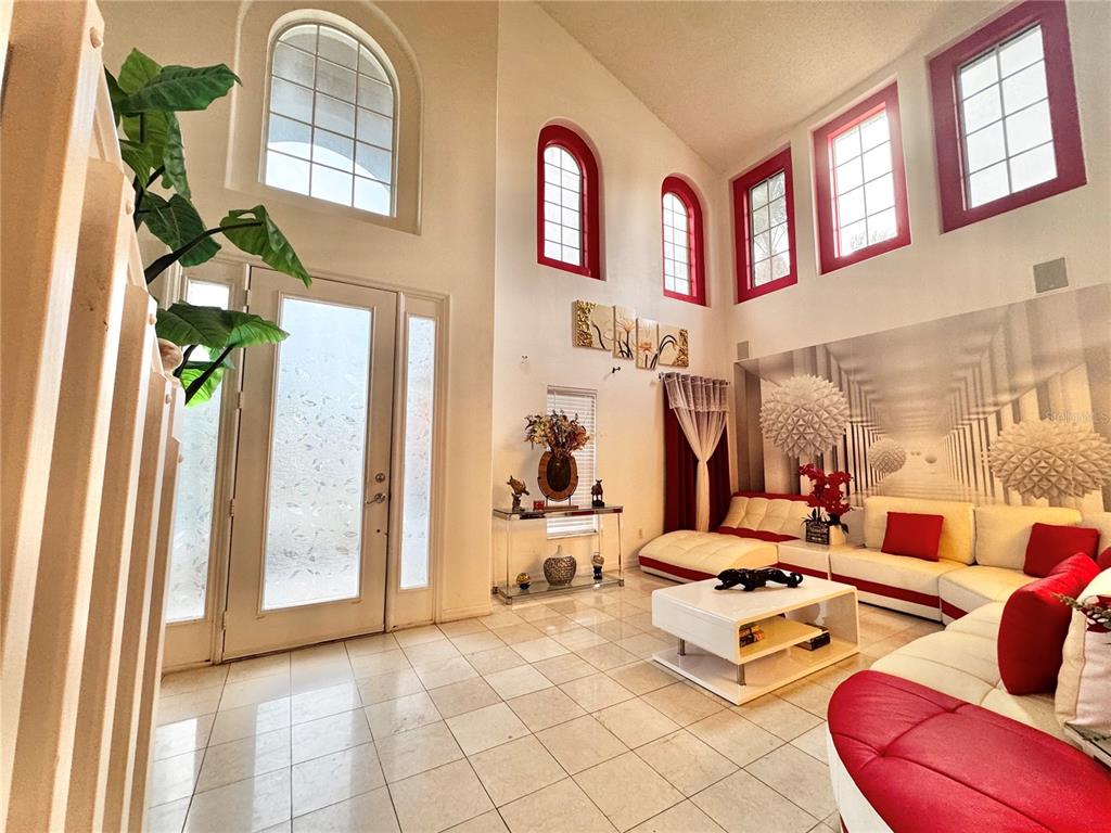 A high-ceilinged living room features white tile floors, red-trimmed windows, and a white sectional sofa — 2561 THE OAKS BOULEVARD, KISSIMMEE, FL