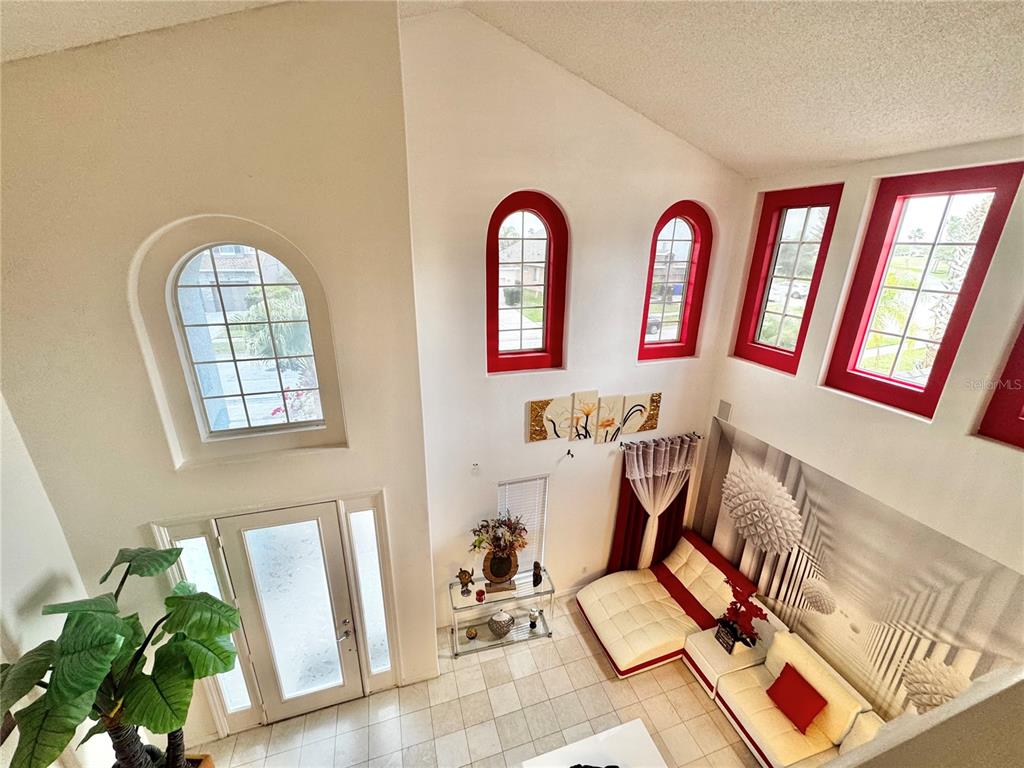 A high-ceilinged living room features white walls, tile floors, red-trimmed windows, and a sectional sofa — 2561 THE OAKS BOULEVARD, KISSIMMEE, FL