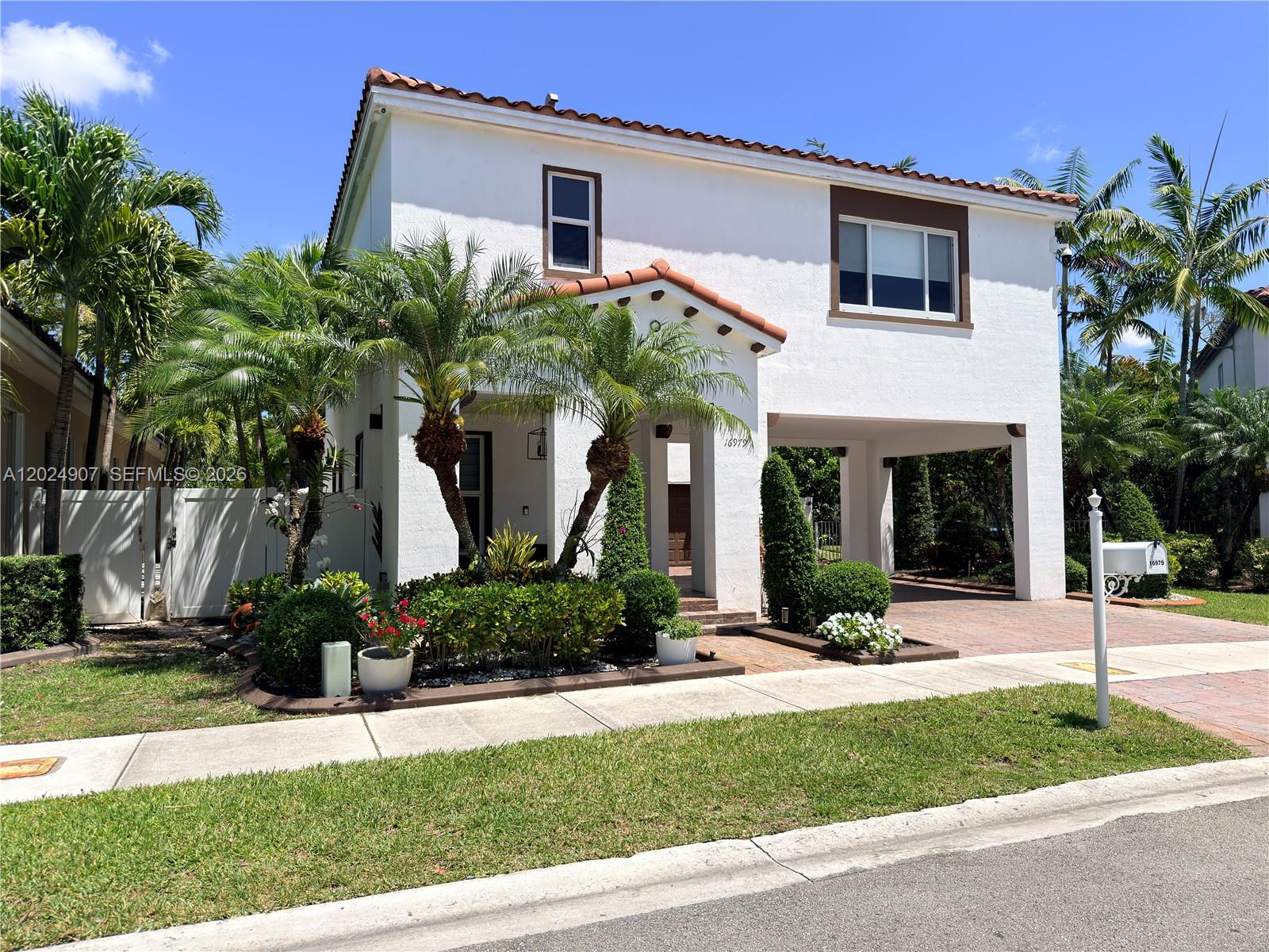 A two-story white stucco house features a tiled roof, palm trees, and a covered carport — MIAMI, FL