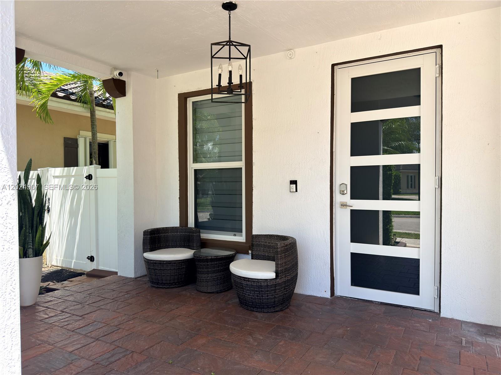 A covered porch features a white front door, a window, and two wicker chairs — MIAMI, FL