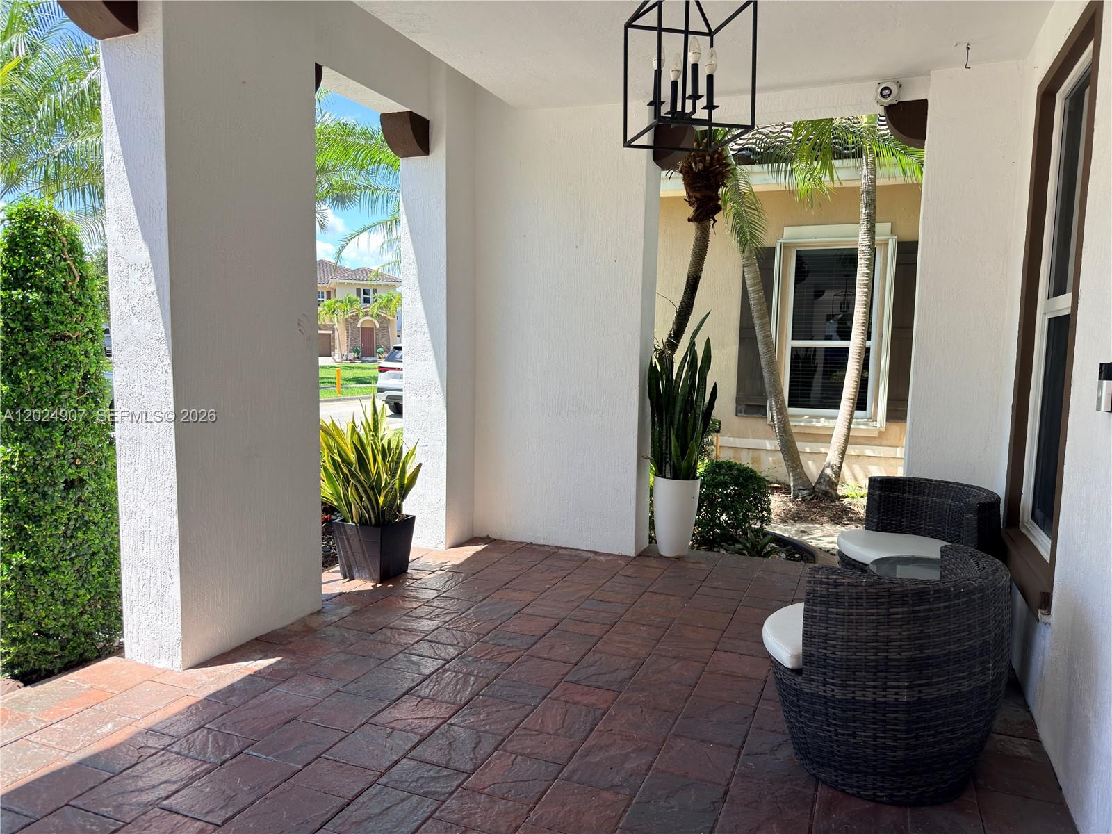 A covered patio features brick pavers, white pillars, wicker chairs, and potted plants — MIAMI, FL