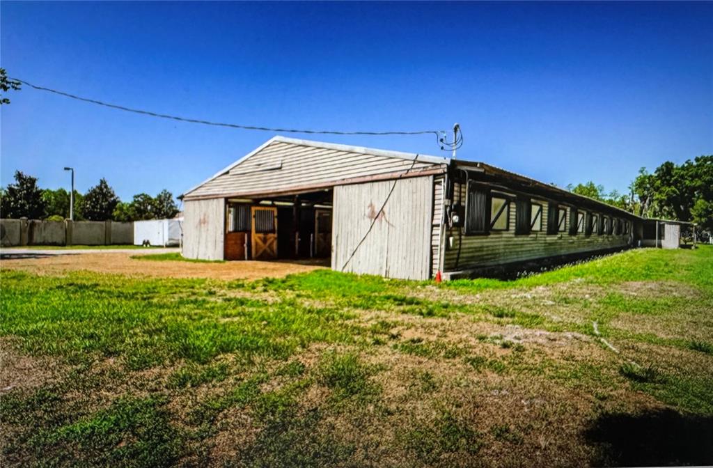A long, single-story barn with wooden siding and multiple stall openings sits on a grassy lot — 10502 HENDERSON ROAD, TAMPA, FL