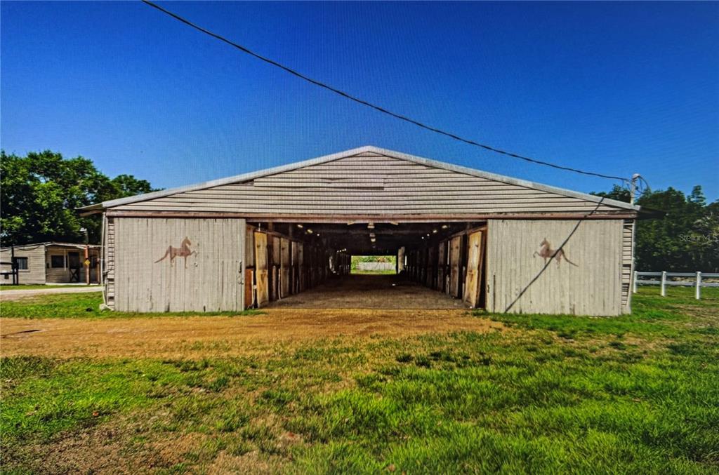 A wide, open-air horse barn with multiple stalls and horse silhouettes painted on the exterior — 10502 HENDERSON ROAD, TAMPA, FL