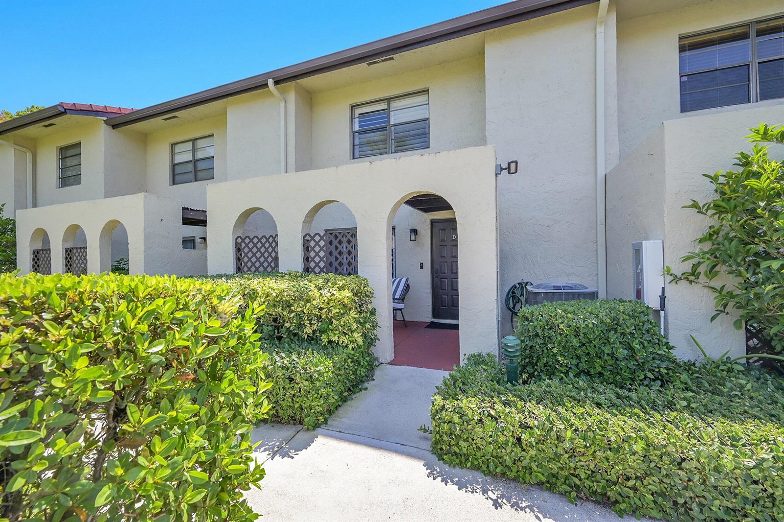 A two-story townhouse exterior features arched entryways, a concrete walkway, and manicured green hedges — 21207 Lago Circle, Boca Raton FL 33433, BOCA RATON, FL