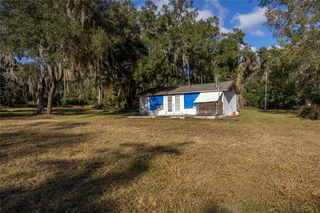 A small, single-story white house with blue window coverings sits on a large grassy lot — 560 NW 39TH ROAD, GAINESVILLE, FL