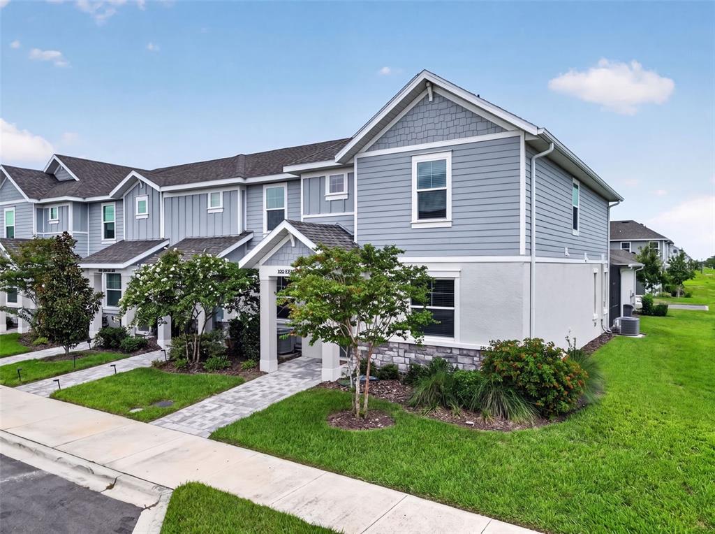 A two-story townhouse with gray siding, stone accents, and a paved walkway leading to the entrance — 1813 FENDER LANE, SARASOTA, FL