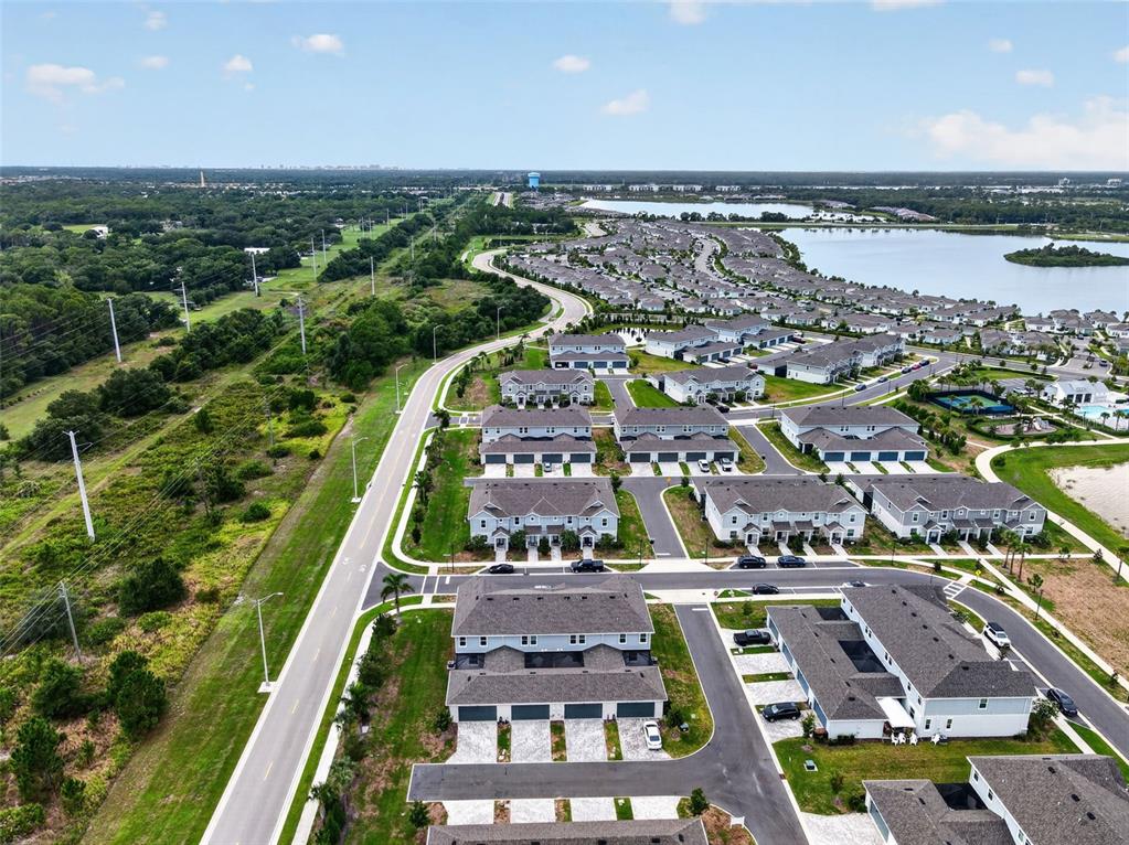 An aerial view shows a suburban neighborhood with townhomes, a winding road, and a lake — 1813 FENDER LANE, SARASOTA, FL