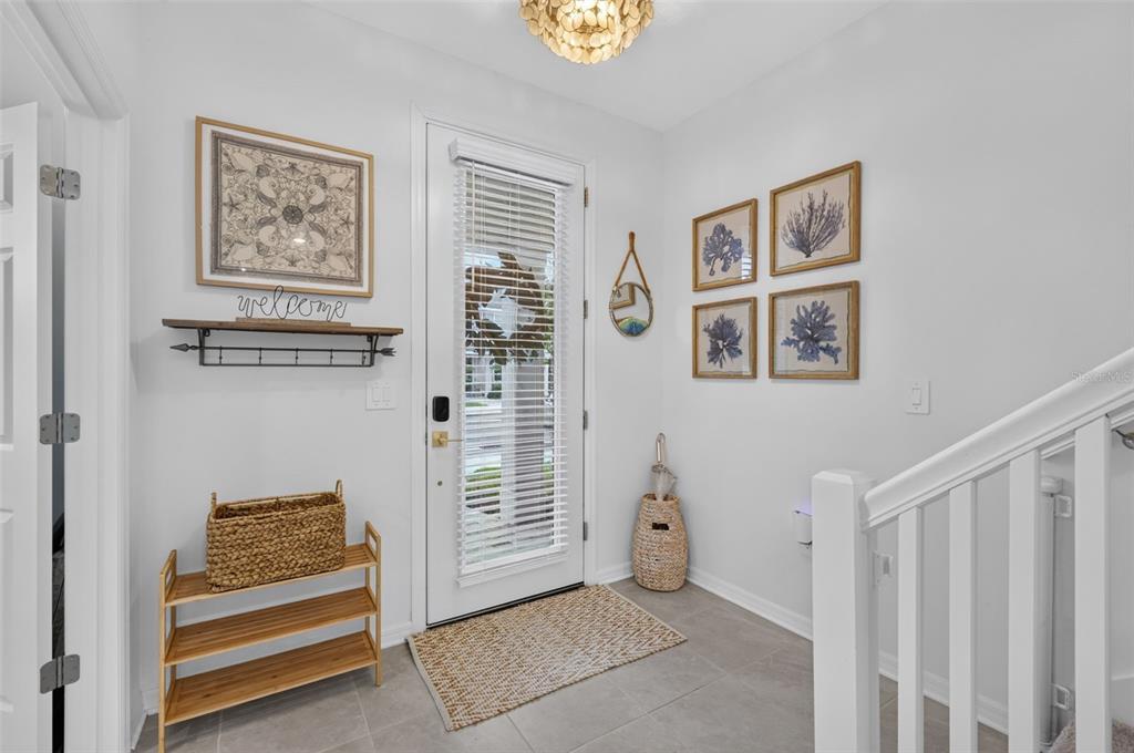 A bright entryway features a glass-paneled door, a wooden shoe rack, and coastal-themed wall art — 1813 FENDER LANE, SARASOTA, FL
