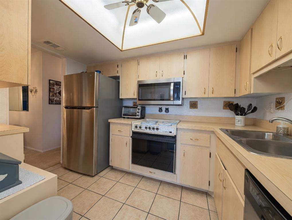 A kitchen features light wood cabinets, stainless steel appliances, and beige tile flooring — 2225 ORANGE BLOSSOM LANE, BRADENTON, FL