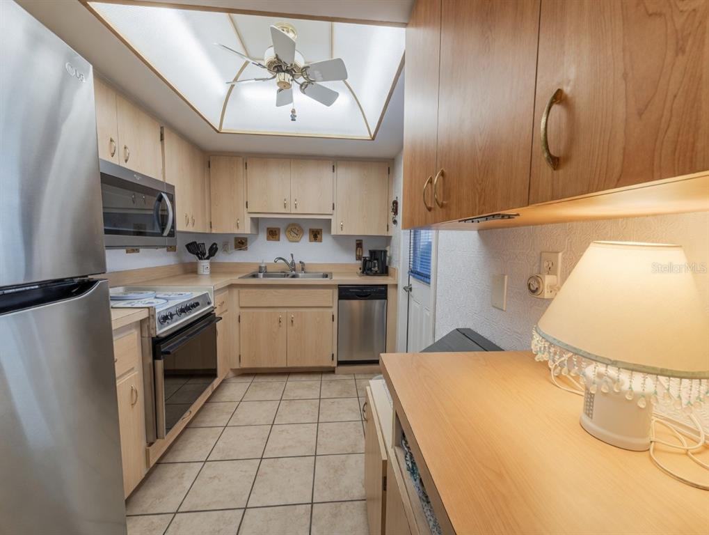 A kitchen features light wood cabinets, stainless steel appliances, tile flooring, and a ceiling fan — 2225 ORANGE BLOSSOM LANE, BRADENTON, FL