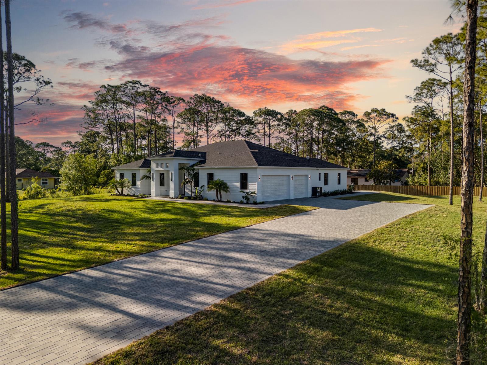 A white single-story house with a paved driveway and a large lawn at sunset — 17975 81st Lane N, Loxahatchee FL 33470, LOXAHATCHEE, FL