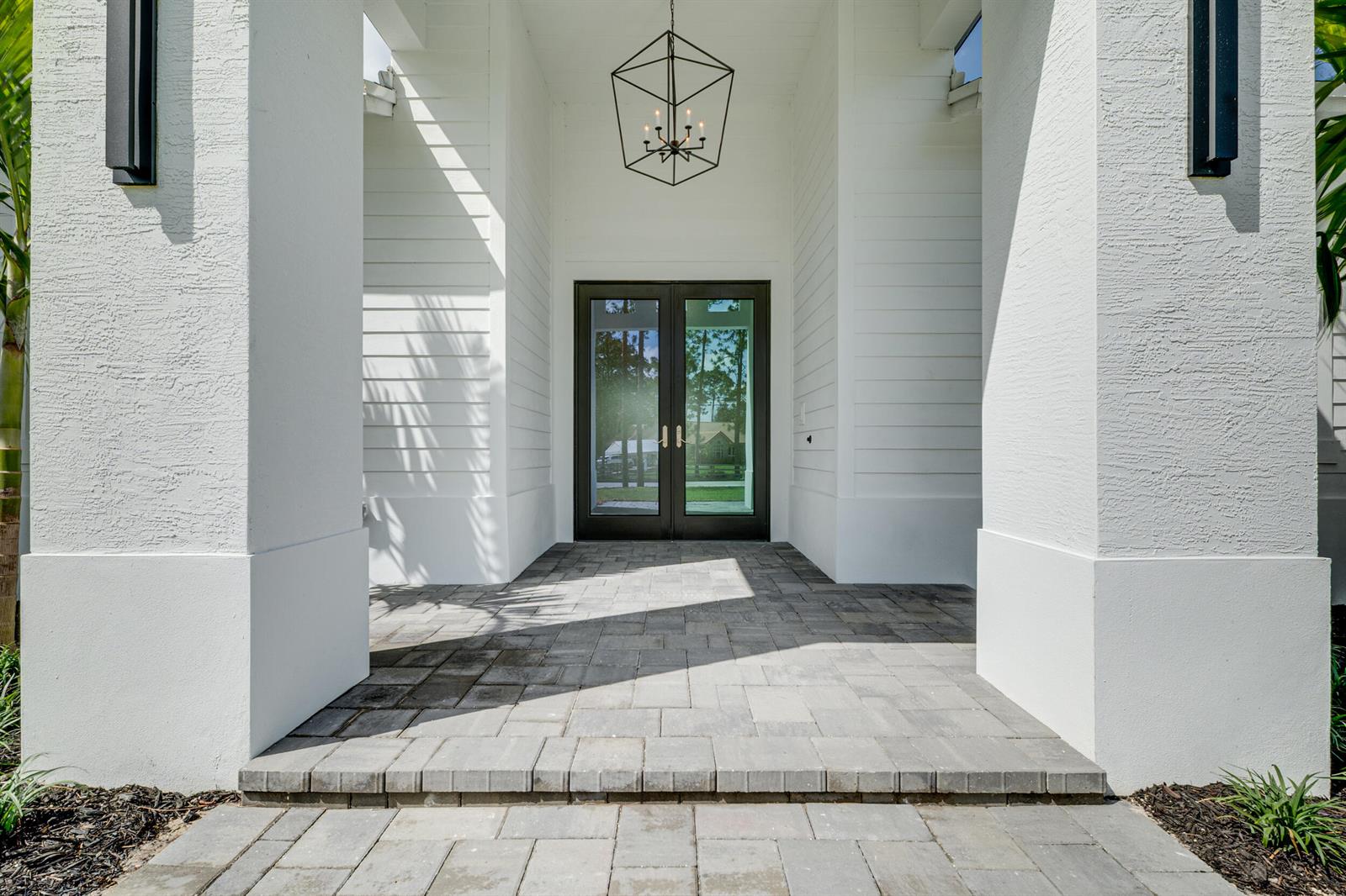 A covered entryway features a paved porch, white horizontal siding, and a modern geometric chandelier — 17975 81st Lane N, Loxahatchee FL 33470, LOXAHATCHEE, FL
