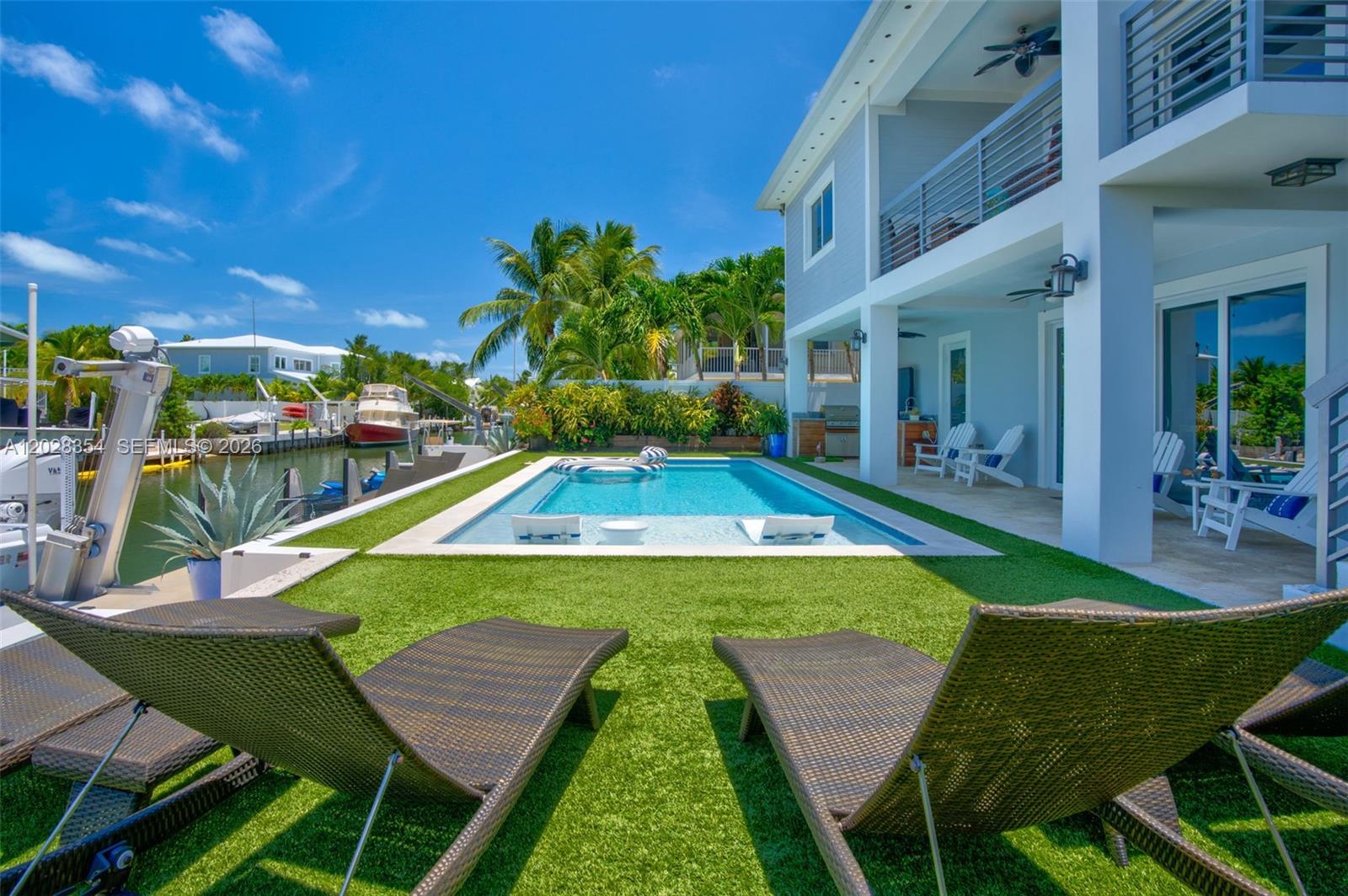 A backyard features a swimming pool, artificial turf, lounge chairs, and a waterfront boat dock — 145 Venetian Drive, Islamorada FL 33036, ISLAMORADA, FL