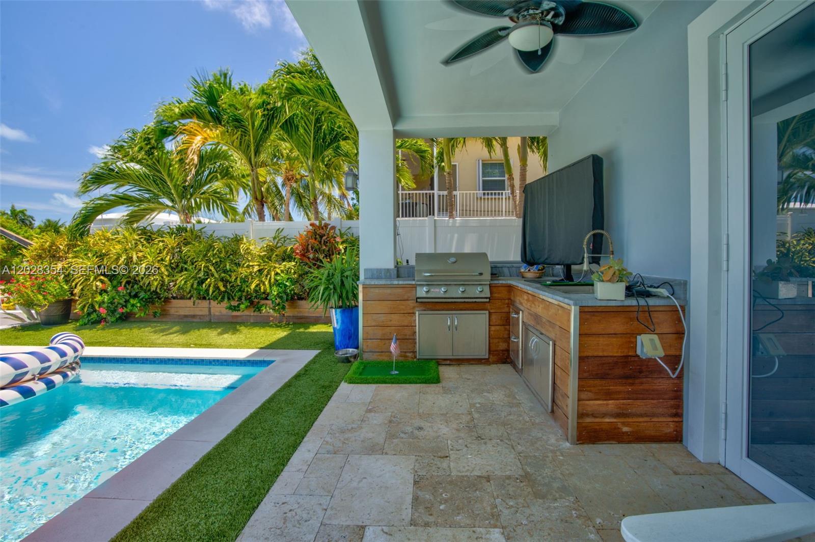 An outdoor kitchen with a grill and stone patio sits beside a swimming pool — 145 Venetian Drive, Islamorada FL 33036, ISLAMORADA, FL