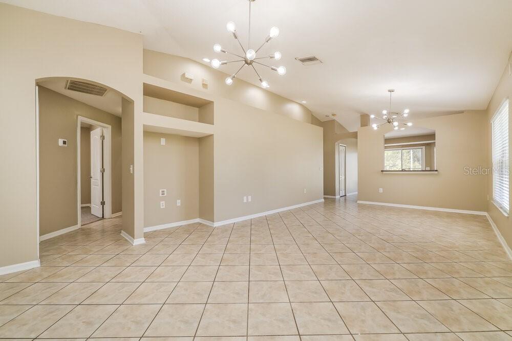 A spacious living area features beige walls, tile flooring, and two modern sputnik-style chandeliers — 12704 EVINGTON POINT DRIVE, RIVERVIEW, FL
