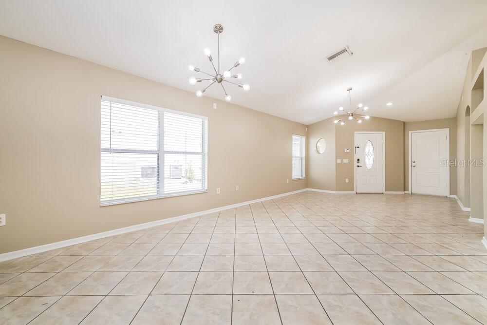 An empty living room with beige walls, tile flooring, and two modern sputnik chandeliers — 12704 EVINGTON POINT DRIVE, RIVERVIEW, FL