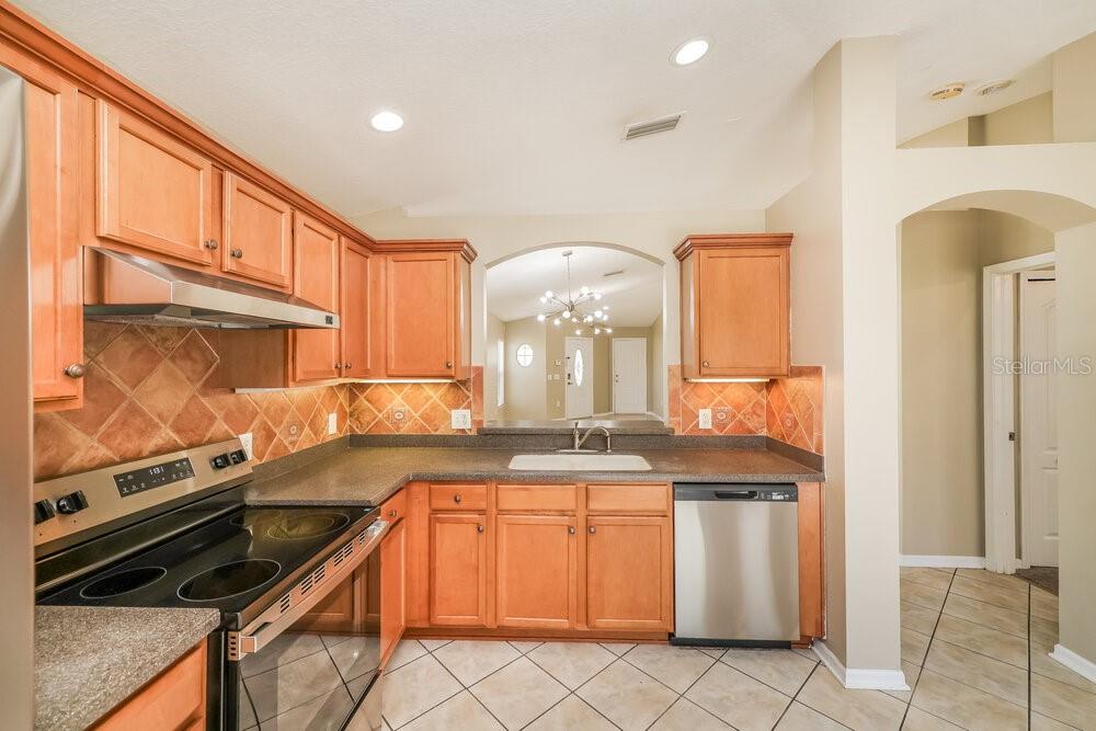 A kitchen with light wood cabinets, dark countertops, tile backsplash, and stainless steel appliances — 12704 EVINGTON POINT DRIVE, RIVERVIEW, FL