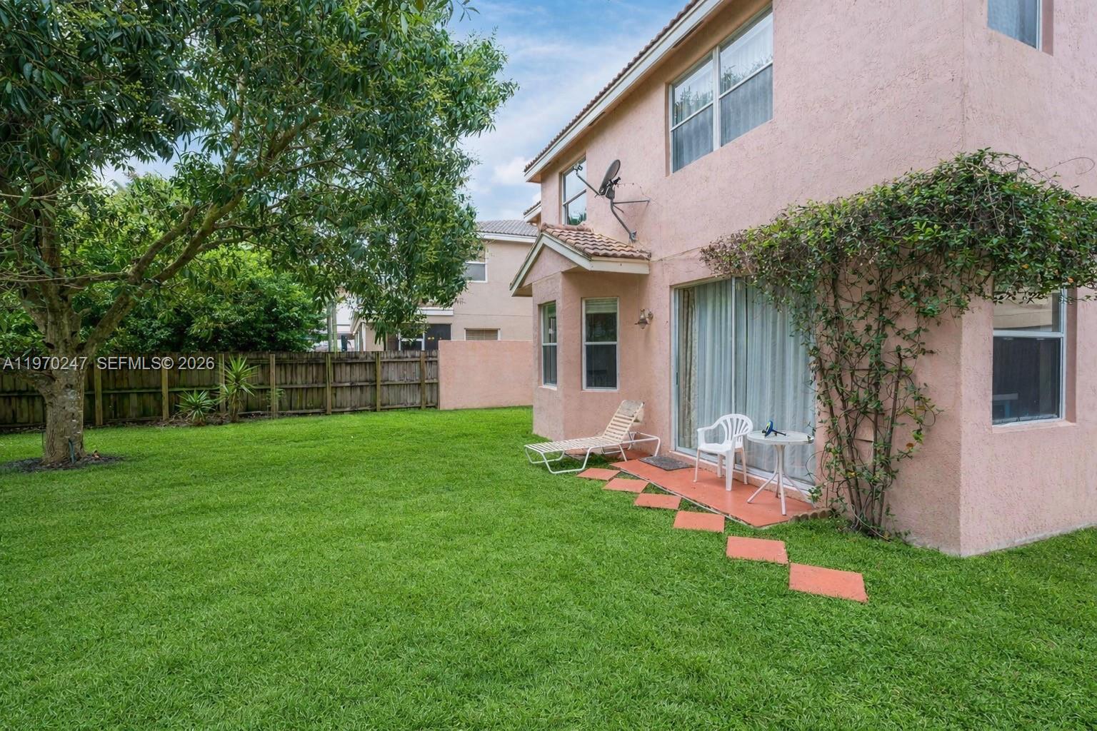 A pink two-story house features a grassy backyard, a patio, and a wooden fence — 9480 Baritone Ct, Boca Raton FL 33496, BOCA RATON, FL
