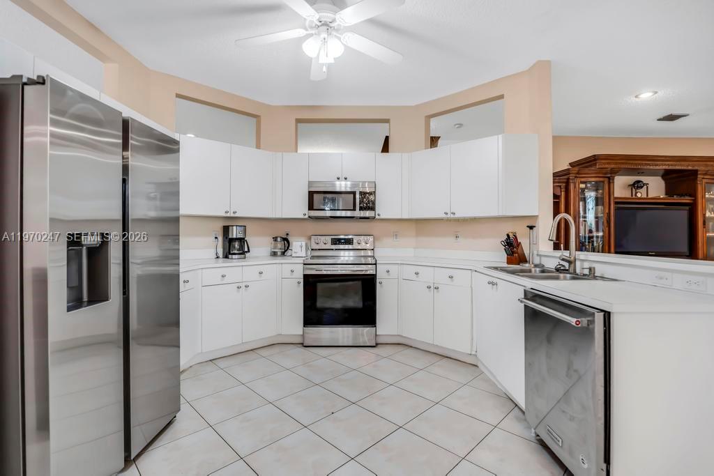 A kitchen with white cabinets, stainless steel appliances, and tile flooring opens to a dining area — 9480 Baritone Ct, Boca Raton FL 33496, BOCA RATON, FL