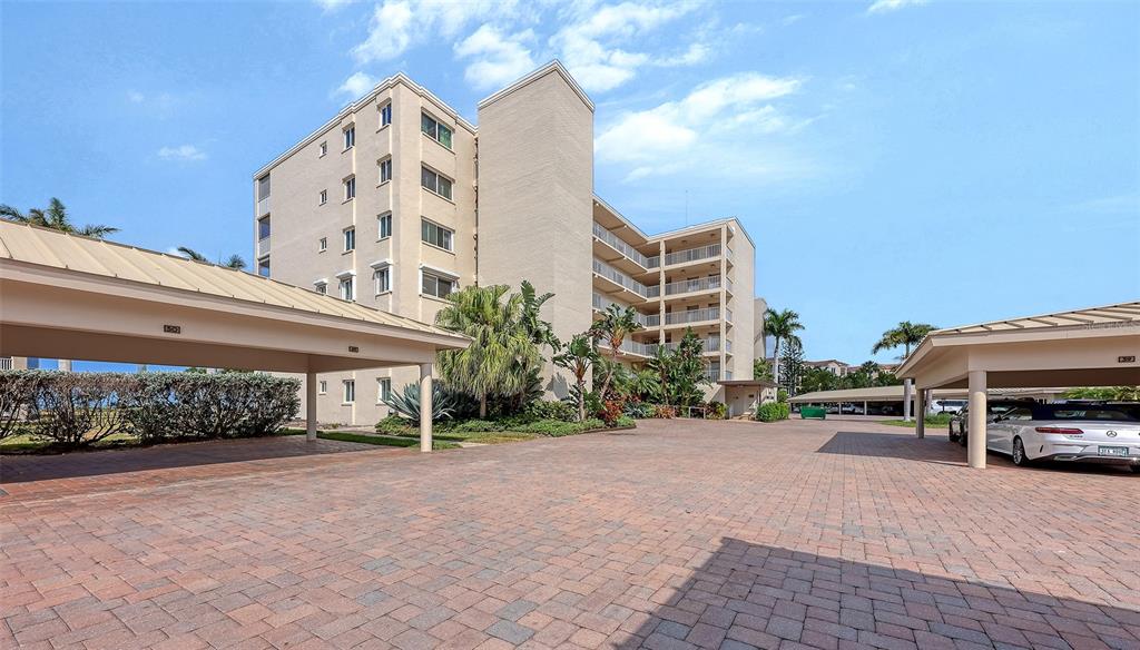 A multi-story apartment building features covered parking structures and a brick-paved driveway — 4825 GULF OF MEXICO DRIVE UNIT 504, LONGBOAT KEY, FL