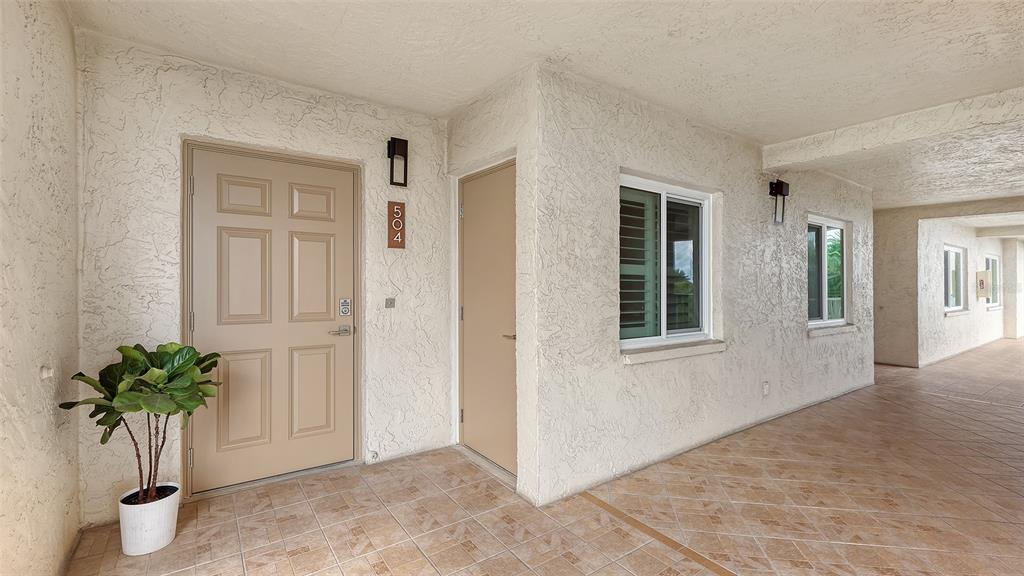 An exterior view of a building entrance with a beige door, tile flooring, and stucco walls — 4825 GULF OF MEXICO DRIVE UNIT 504, LONGBOAT KEY, FL