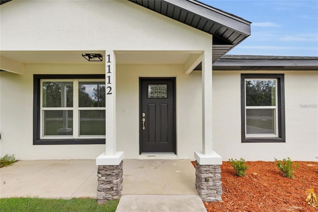 The exterior of a house features a covered porch, a dark front door, and stone-based columns — 14619 SW 21 PLACE, OCALA, FL