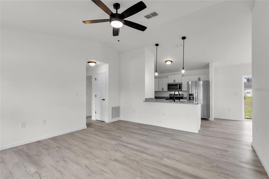 An open-concept living room and kitchen featuring white walls, wood-look flooring, and stainless steel appliances — 14619 SW 21 PLACE, OCALA, FL