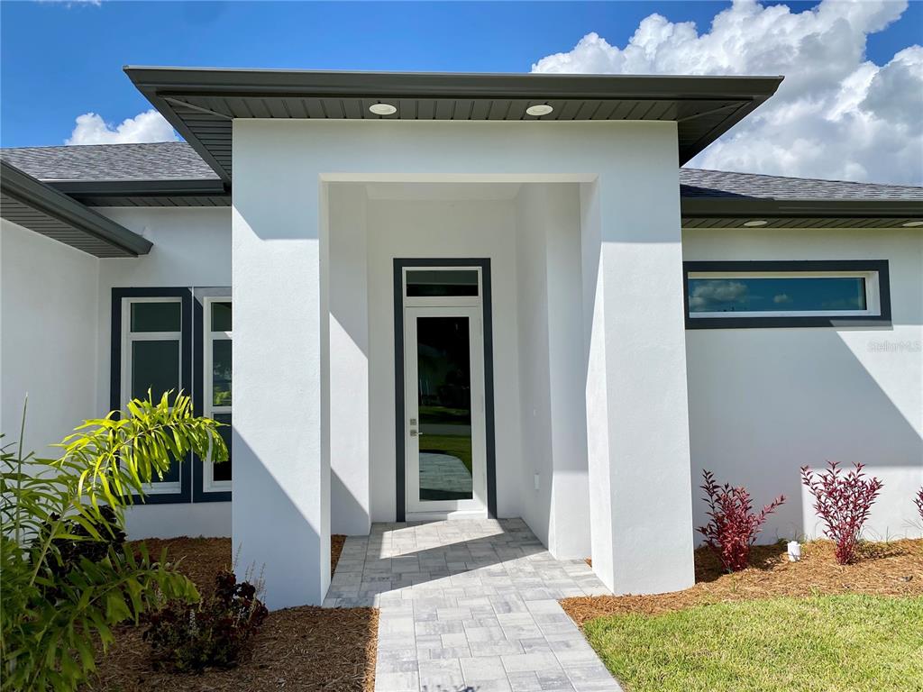 The exterior of a modern white home features a glass front door and stone walkway — 23466 GARRETT AVENUE, PORT CHARLOTTE, FL