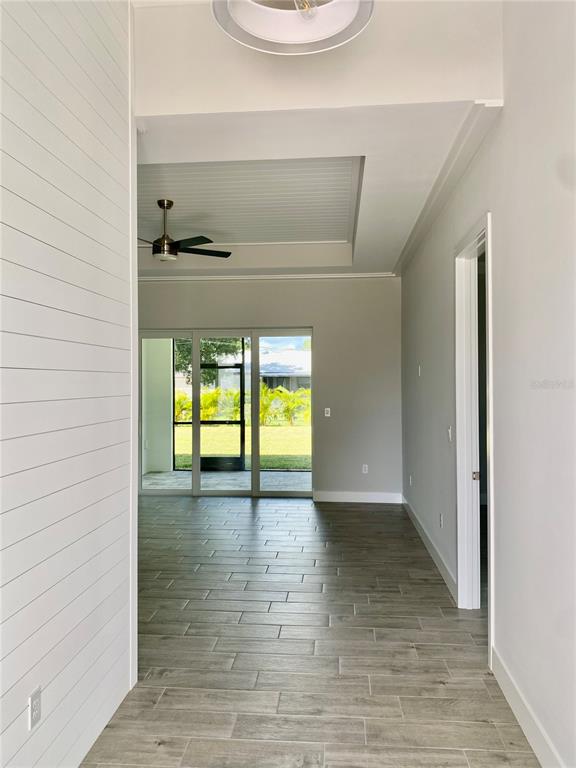 A hallway with shiplap walls leads to a living area with a tray ceiling — 23466 GARRETT AVENUE, PORT CHARLOTTE, FL