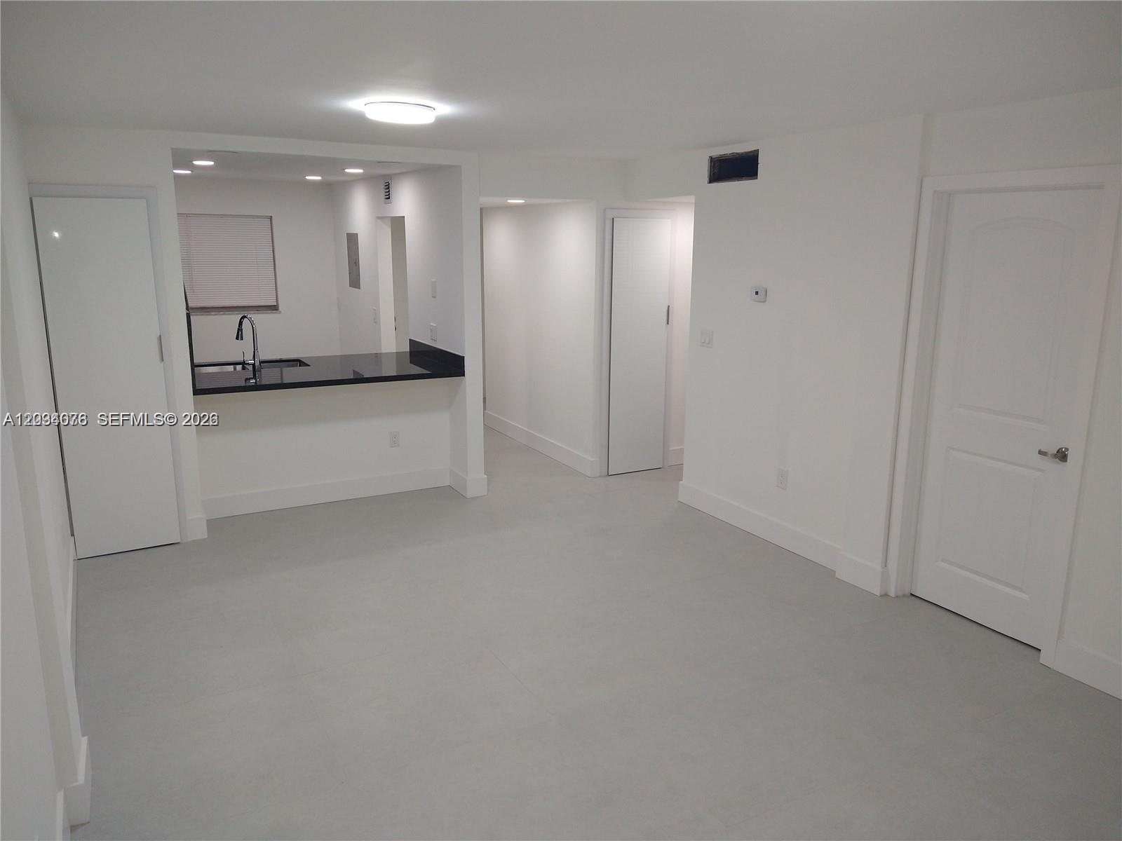 A minimalist room features white walls, gray tile flooring, and a kitchen pass-through window — 19791 SW 114th Ave # 233, Miami FL 33157, MIAMI, FL
