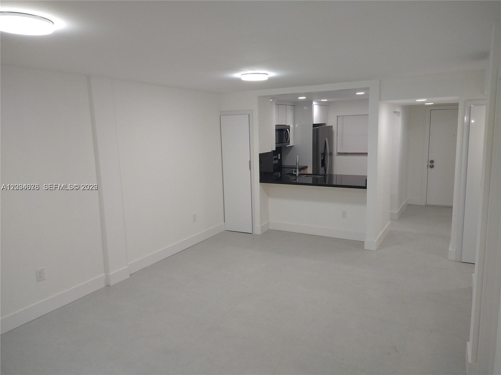 An empty room with white walls and light tile flooring features an open kitchen pass-through — 19791 SW 114th Ave # 233, Miami FL 33157, MIAMI, FL