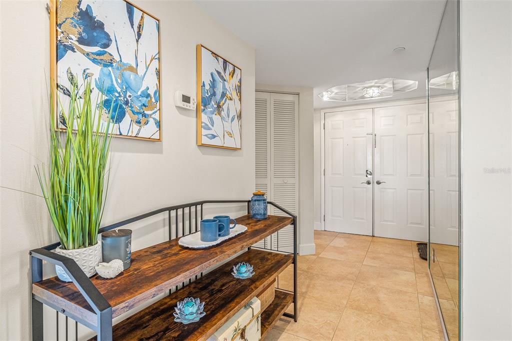An entryway features a wooden console table, wall art, and double doors on tiled flooring — 1310 GULF BOULEVARD UNIT 10D, CLEARWATER BEACH, FL