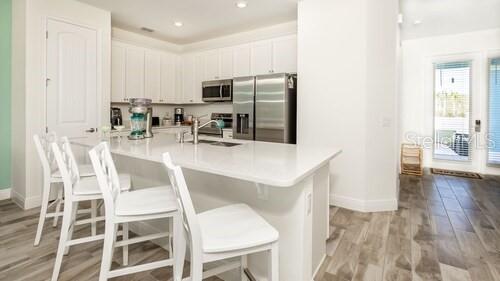A modern kitchen features white cabinetry, stainless steel appliances, and a central island with seating — 8123 COCONUT PLACE, KISSIMMEE, FL