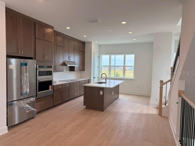 A modern kitchen features brown cabinetry, stainless steel appliances, a center island, and light wood flooring — 9297 LUMINARY BOULEVARD, ORLANDO, FL