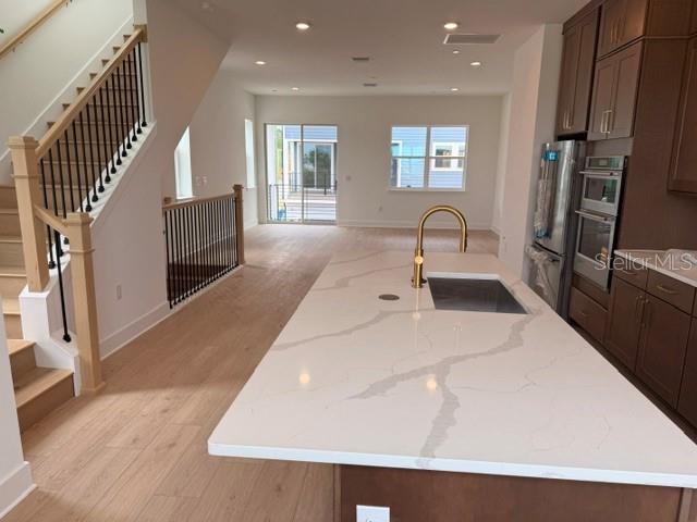 A kitchen with a white quartz island, wood flooring, and a staircase with black railings — 9297 LUMINARY BOULEVARD, ORLANDO, FL