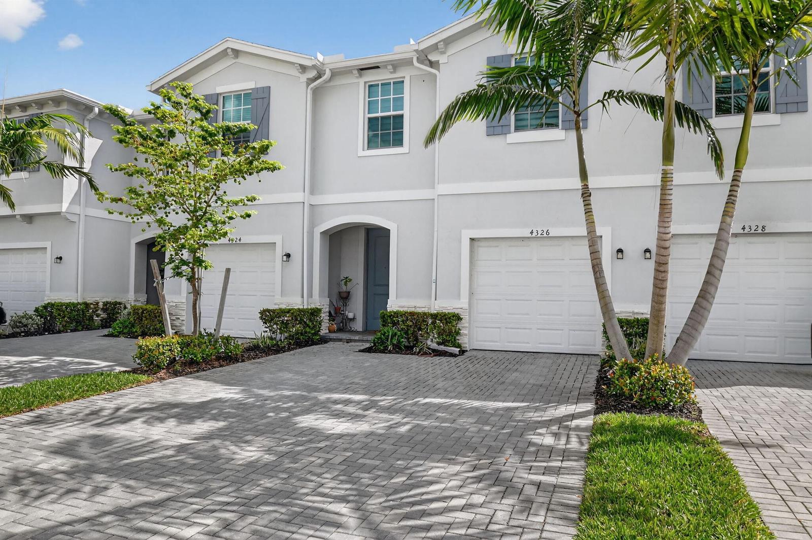 A row of three-story townhouses with gray siding, white garage doors, and a paved driveway — 4326 Hammock Grove Drive, Lake Worth FL 33467, LAKE WORTH, FL