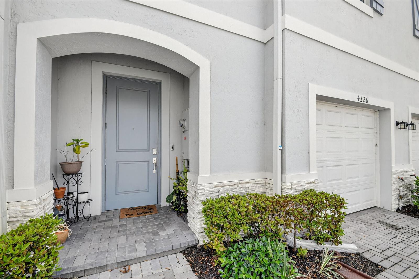The exterior of a gray home features a front door, a garage, and landscaping — 4326 Hammock Grove Drive, Lake Worth FL 33467, LAKE WORTH, FL