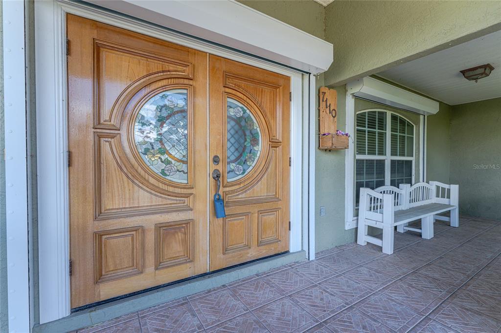 A covered porch features double wooden doors with stained glass accents and a white bench — 7110 SAN CASA DRIVE, ENGLEWOOD, FL