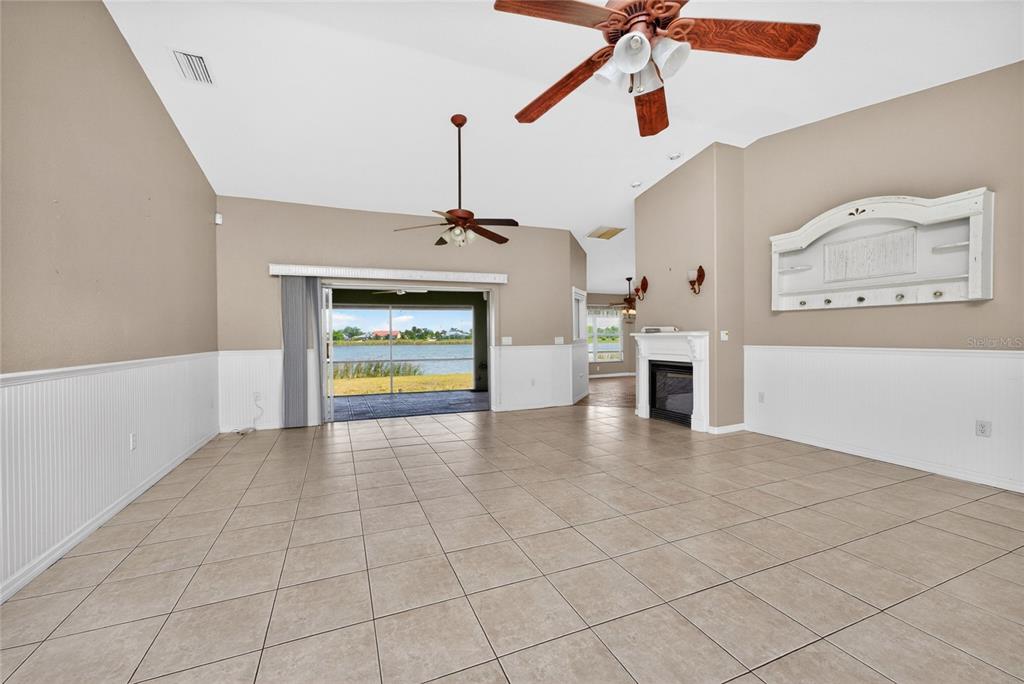 A spacious living room features tile flooring, a fireplace, and a sliding door to a lake — 7110 SAN CASA DRIVE, ENGLEWOOD, FL
