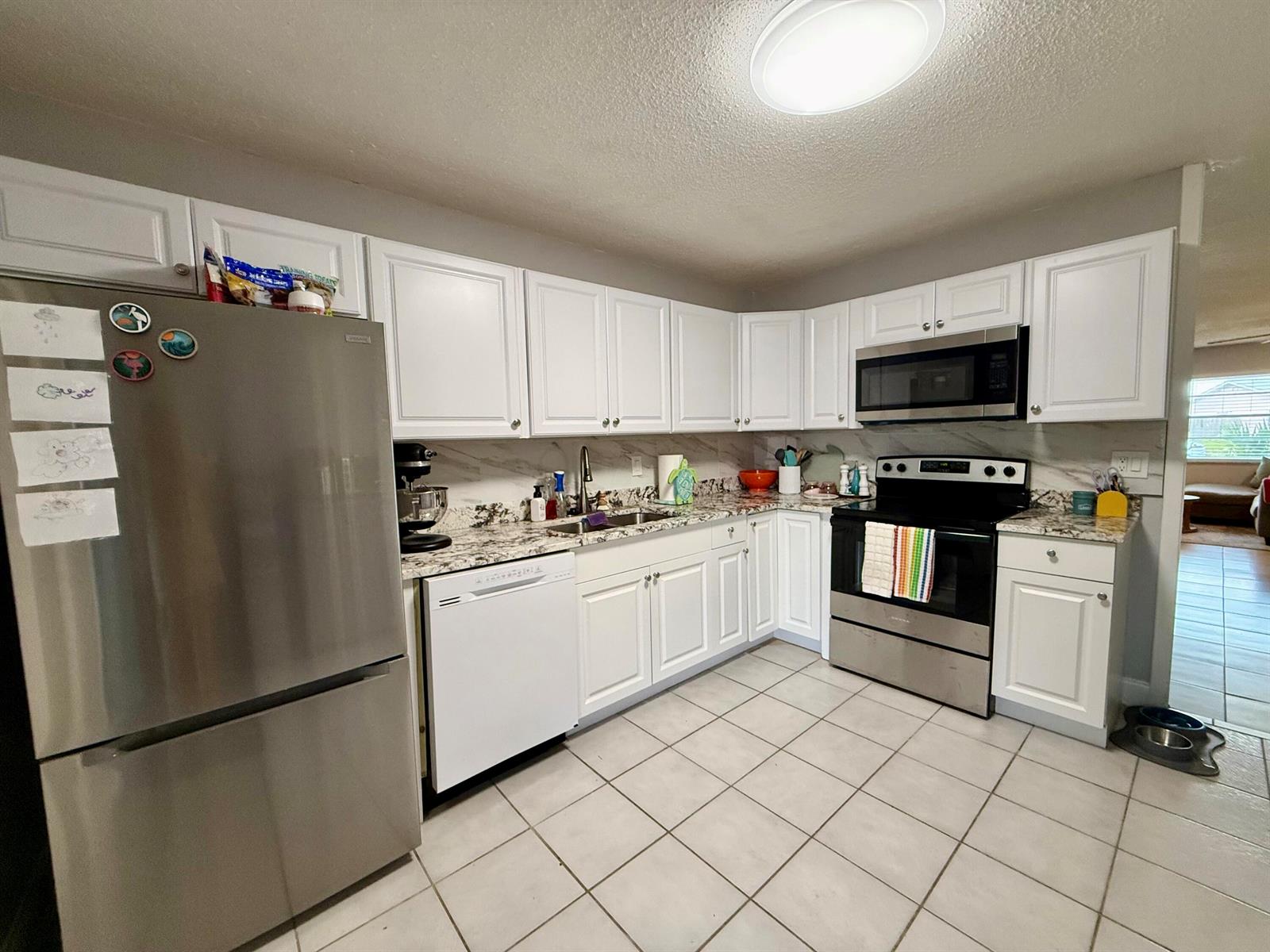 A kitchen features white cabinets, stainless steel appliances, granite countertops, and light-colored tile flooring — 4441-4443 SE Village Road, Stuart FL 34997, STUART, FL